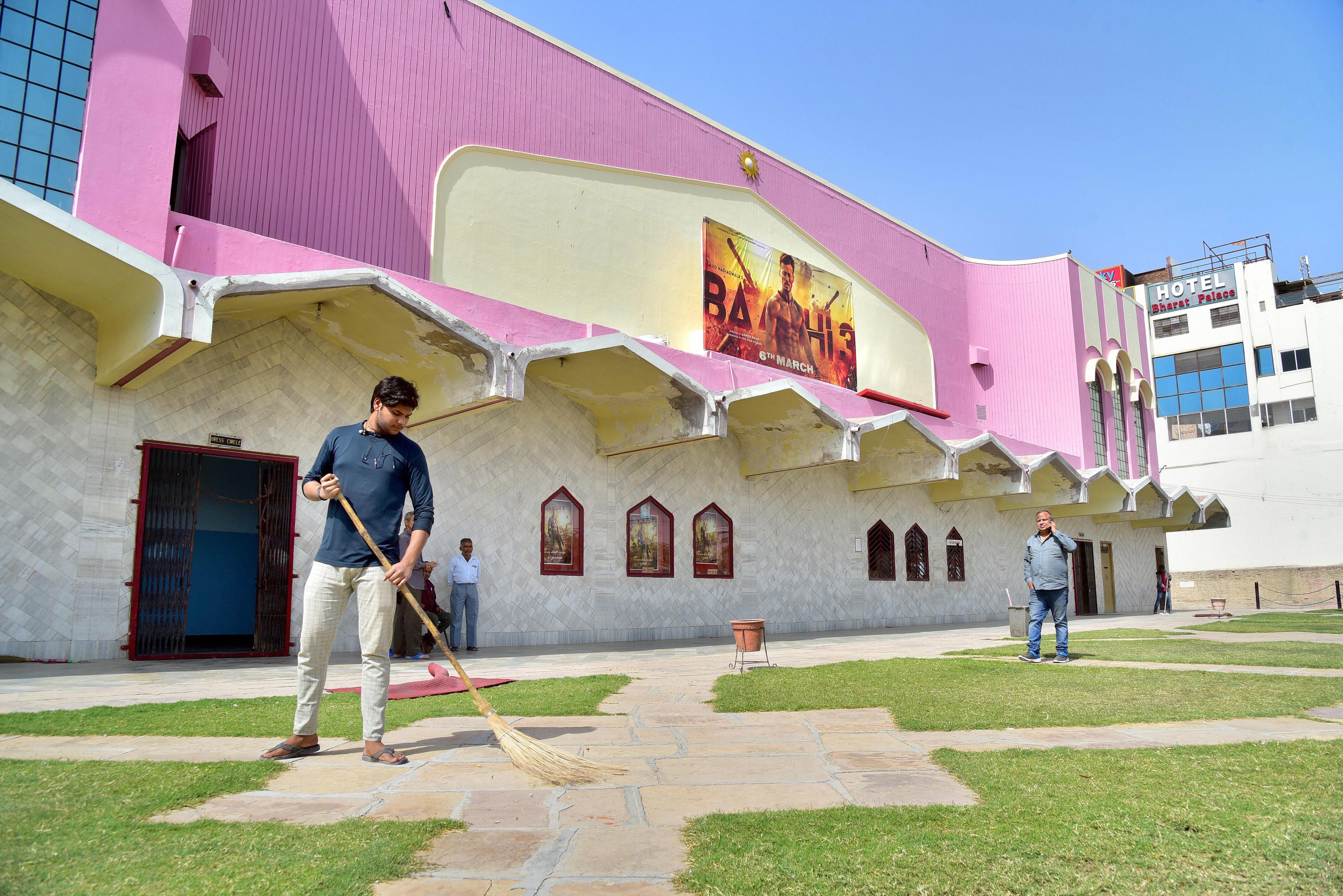 A worker sweeps the lawn of a closed cinema hall in view of the novel coronavirus (COVID-19) outbreak, in Bikaner, Saturday, March 14, 2020.