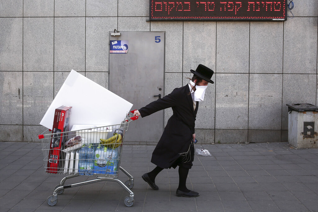 An ultra-Orthodox Jew wears an improvised protective face mask as he pulls a supermarket cart on a mainly deserted street because of the government's measures to help stop the spread of the coronavirus, in Bnei Brak, a suburb of Tel Aviv, Israel, Friday, April 3, 2020. The military plans to send troops in to assist local authorities with coronavirus control.
