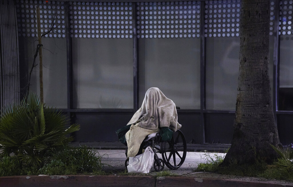 A homeless person sits on a wheelchair under rainy weather on Sunset Blvd., in the Echo Park neighborhood of Los Angeles Monday, April 6, 2020. One population is particularly vulnerable to contracting and spreading the coronavirus: the homeless. 