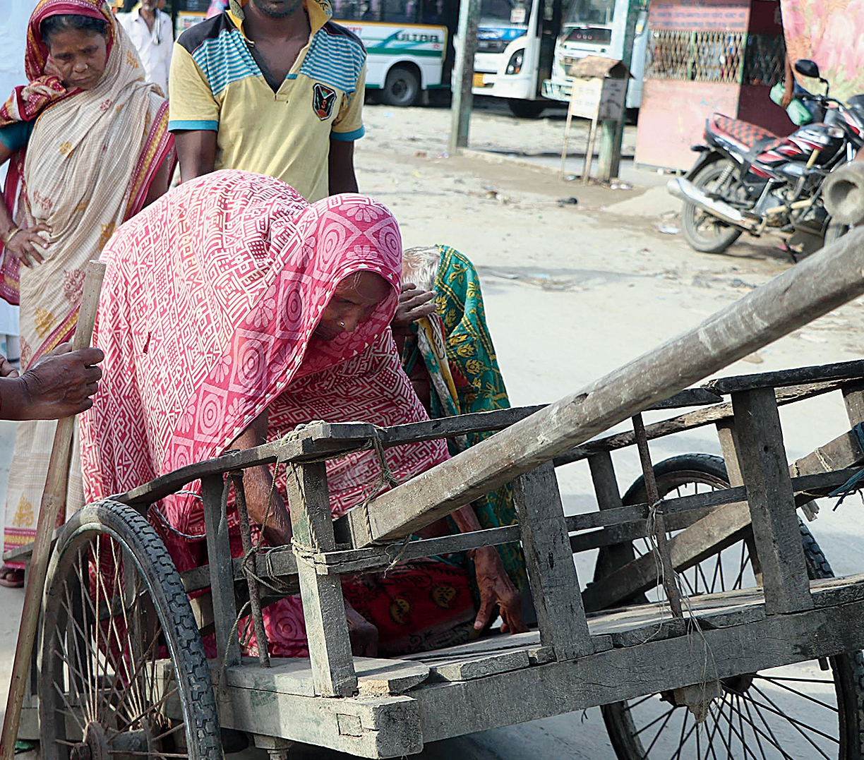 An elderly woman tries to get on a handcart.
