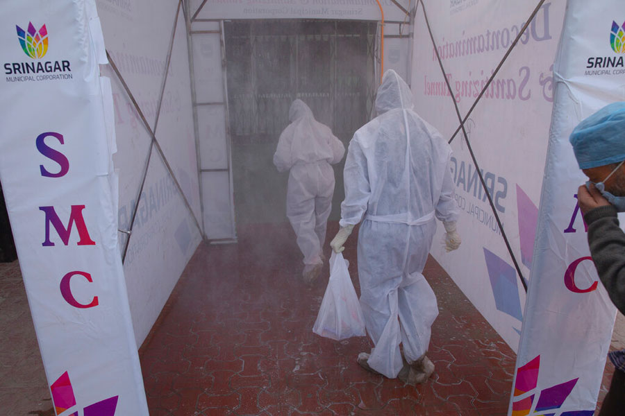 Medical staff wearing protective gear walk inside a disinfecting tunnel outside a hospital where most coronavirus patients are being treated in Srinagar