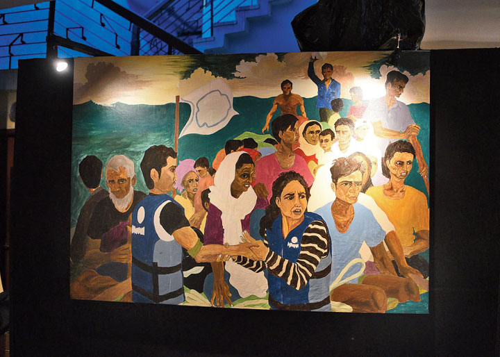 An acrylic painting. Made by Sampurna Pal, the canvas shows a crowded boat in water. There is no caption but the peace flag and the grim faces draw a refugee parallel. “The subject is derived from real-life footage of Rohingyas, Syrian and other refugees,” said Pal.