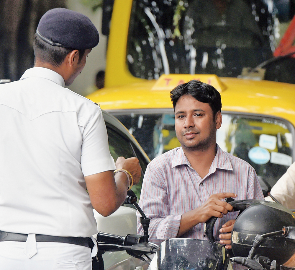 A policeman asks a biker to wear his helmet that was hanging from the handle of his motorcycle on Mayfair Road in Ballygunge