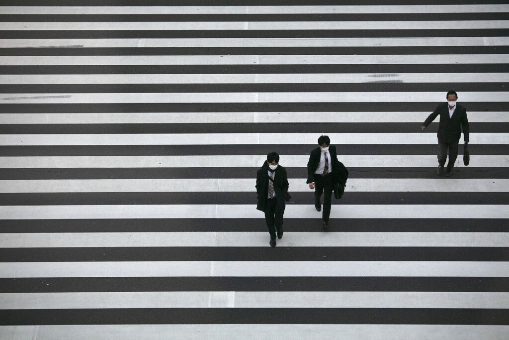 Commuters wearing masks walk across a pedestrian crosswalk Wednesday, in Tokyo