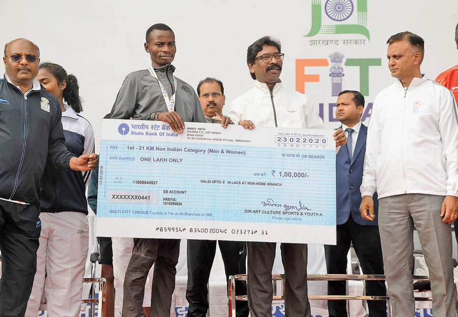 Chief minister Hemant Soren hands over a dummy cheque to Elias Matu Njambi from Kenya, the winner of the 21km run category at the event