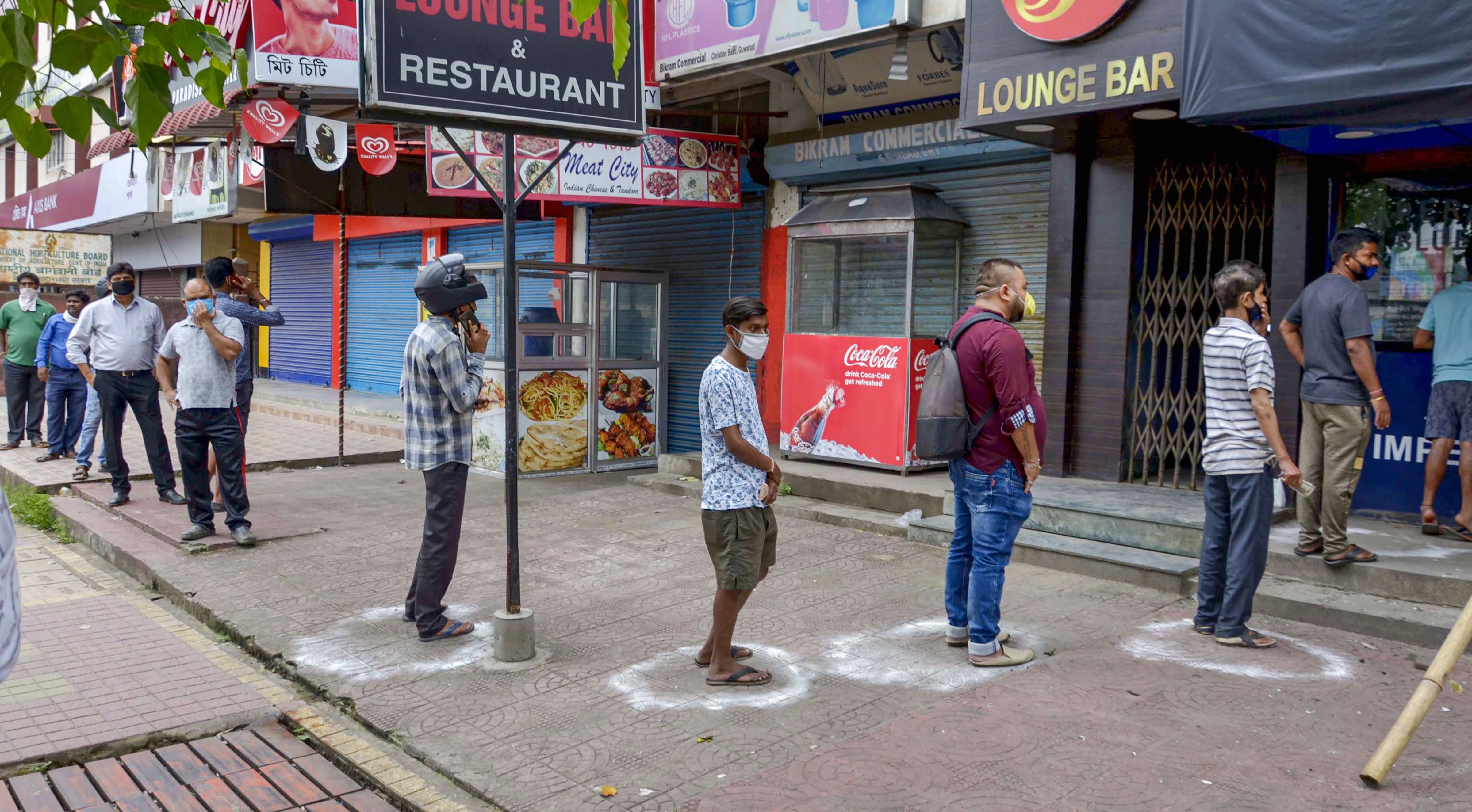 People maintain social distance as they stand in a queue to buy alcohol from a wine shop, during the ongoing Covid-19 pandemic, in Guwahati, Saturday, May 2, 2020.