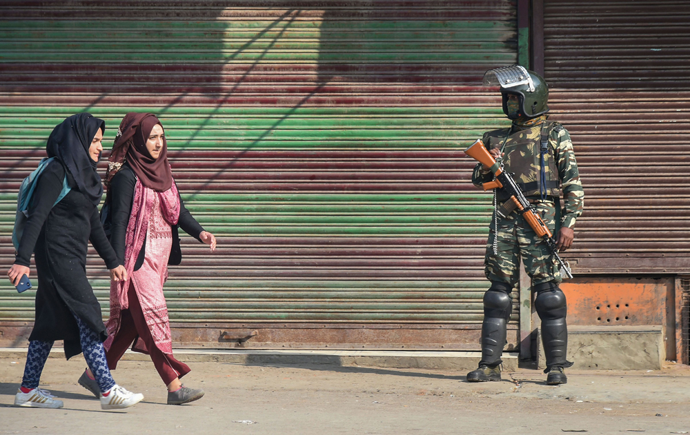 Kashmiri women walk past a security guard in Srinagar on Tuesday