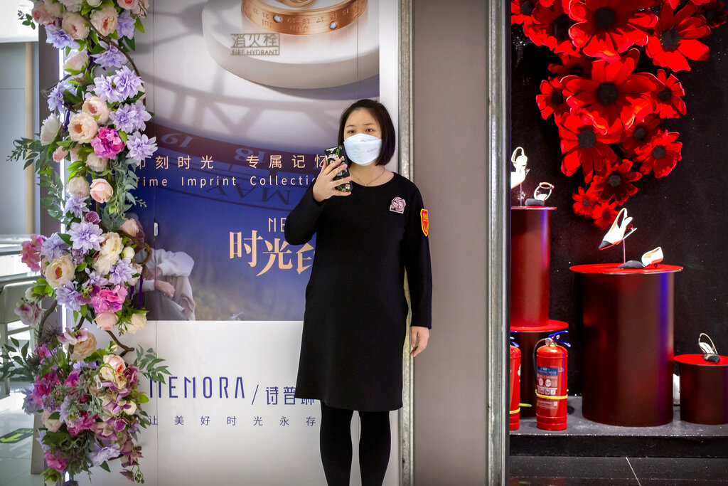 A clerk wears a face mask as she stands outside a store at a mostly empty shopping mall in Beijing, Saturday, March 7, 2020