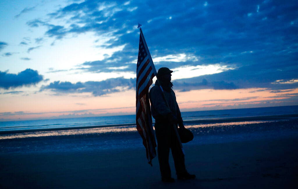 Udo Hartung from Frankfurt, Germany, a World War II re-enactor holds the US flag as he stands at dawn on Omaha Beach, in Normandy, France, Thursday, June 6, 2019 during commemorations of the 75th anniversary of D-Day. 