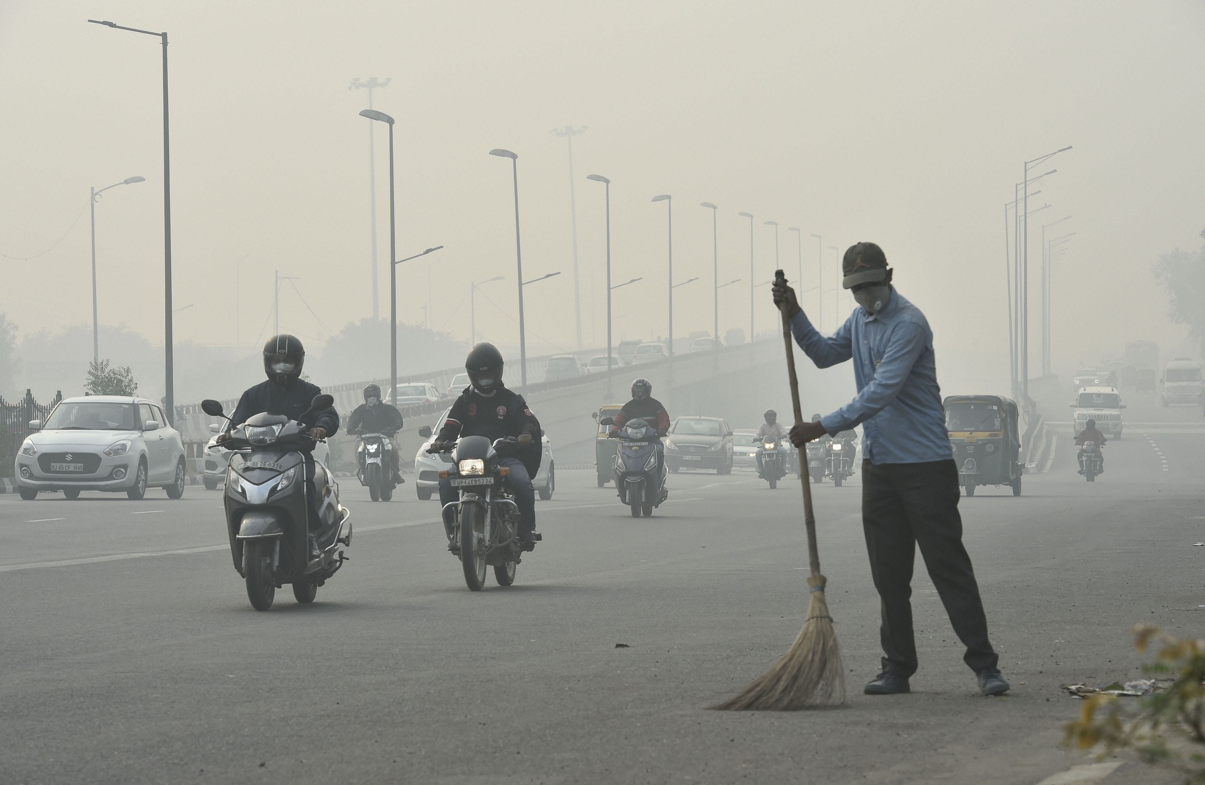 A civic worker, wearing an anti-pollution mask, sweeps the road amid heavy smog, in New Delhi, Friday, Nov. 15, 2019. 