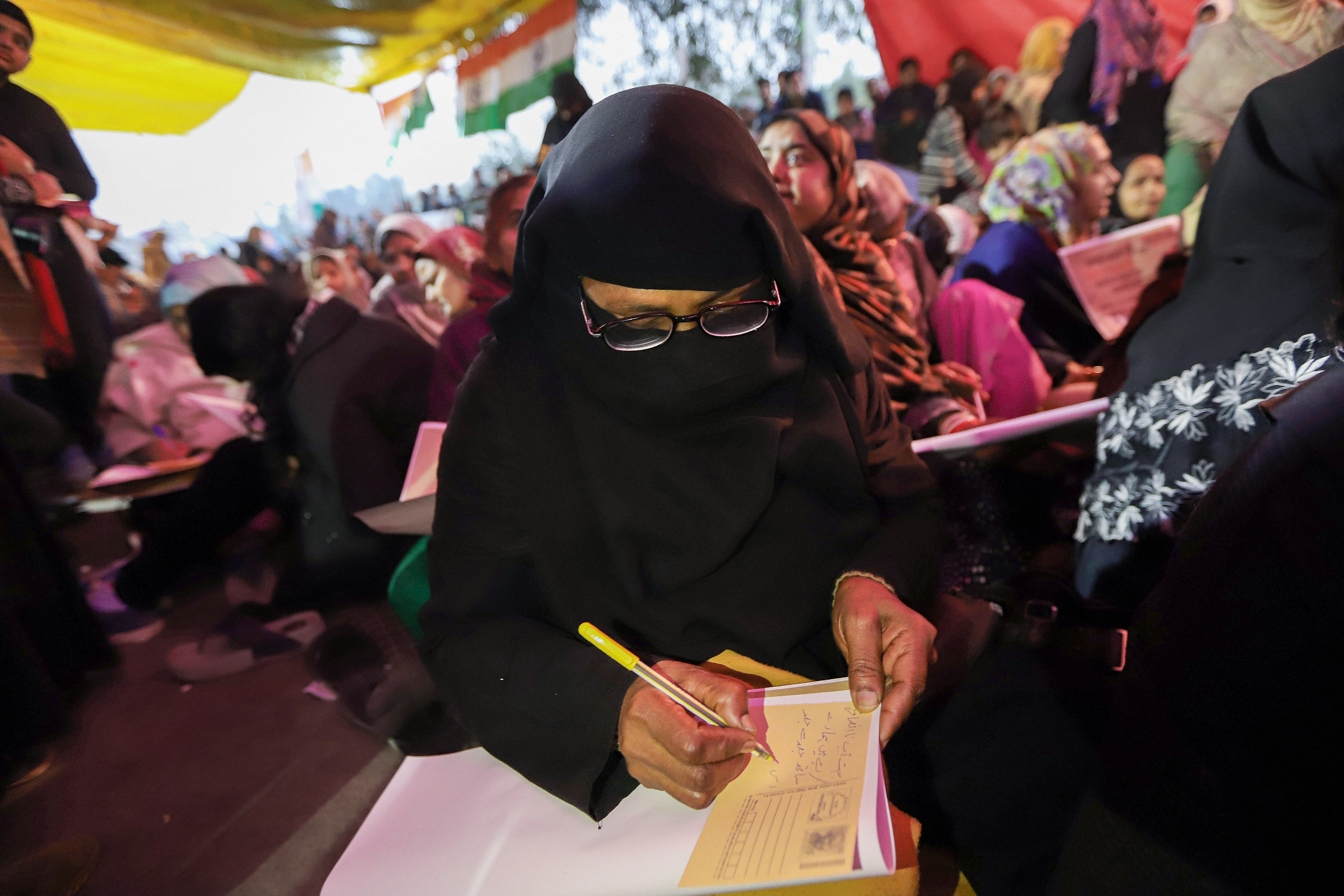 A woman writes a message on a postcard addressed to the Prime Minister during a demonstration against the citizenship (amendment) act and the NRC at Shaheen Bagh on Saturday 
