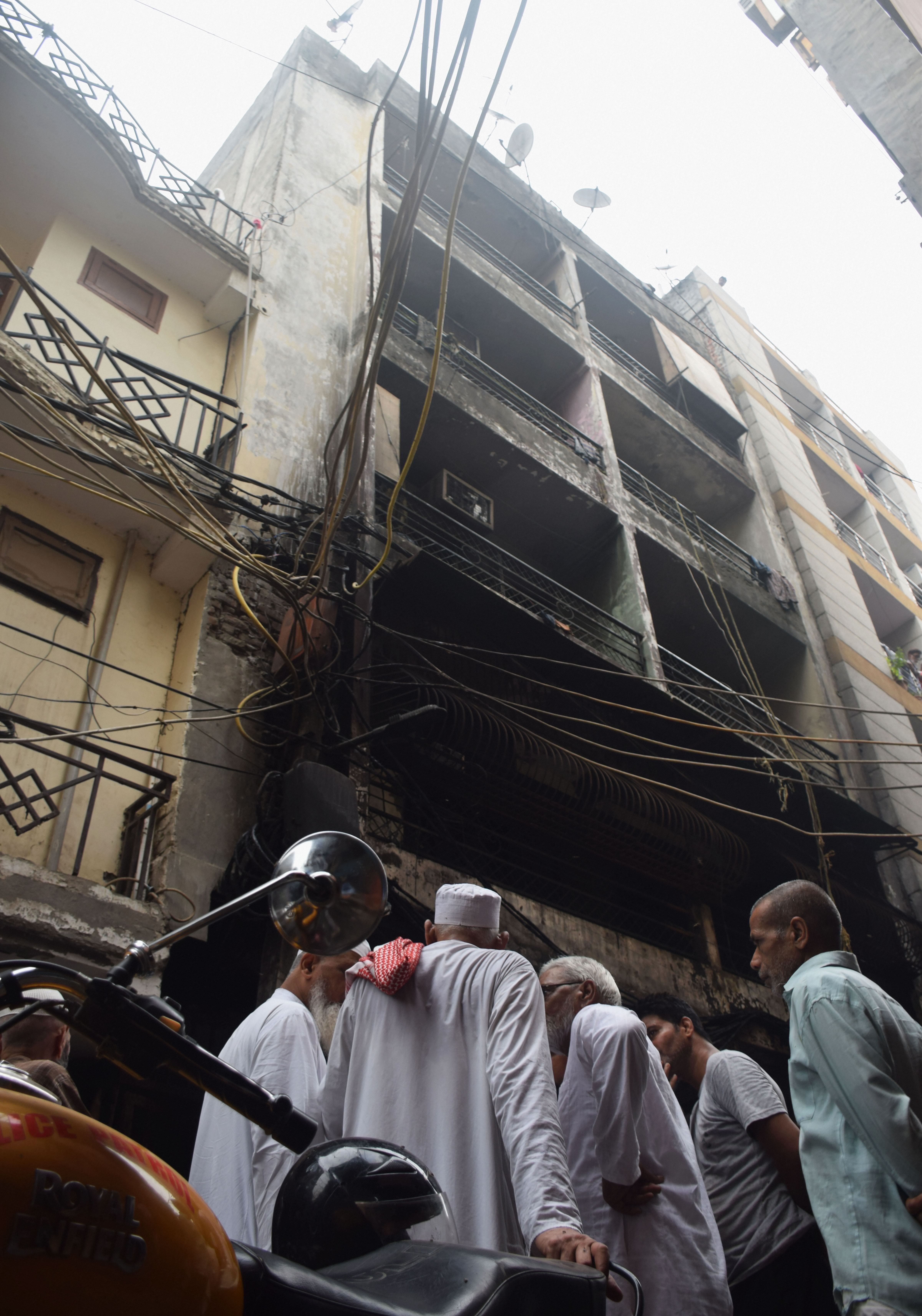 People look at the charred remains of a building at Zakir Nagar  in New Delhi where a fire broke out on August 6.