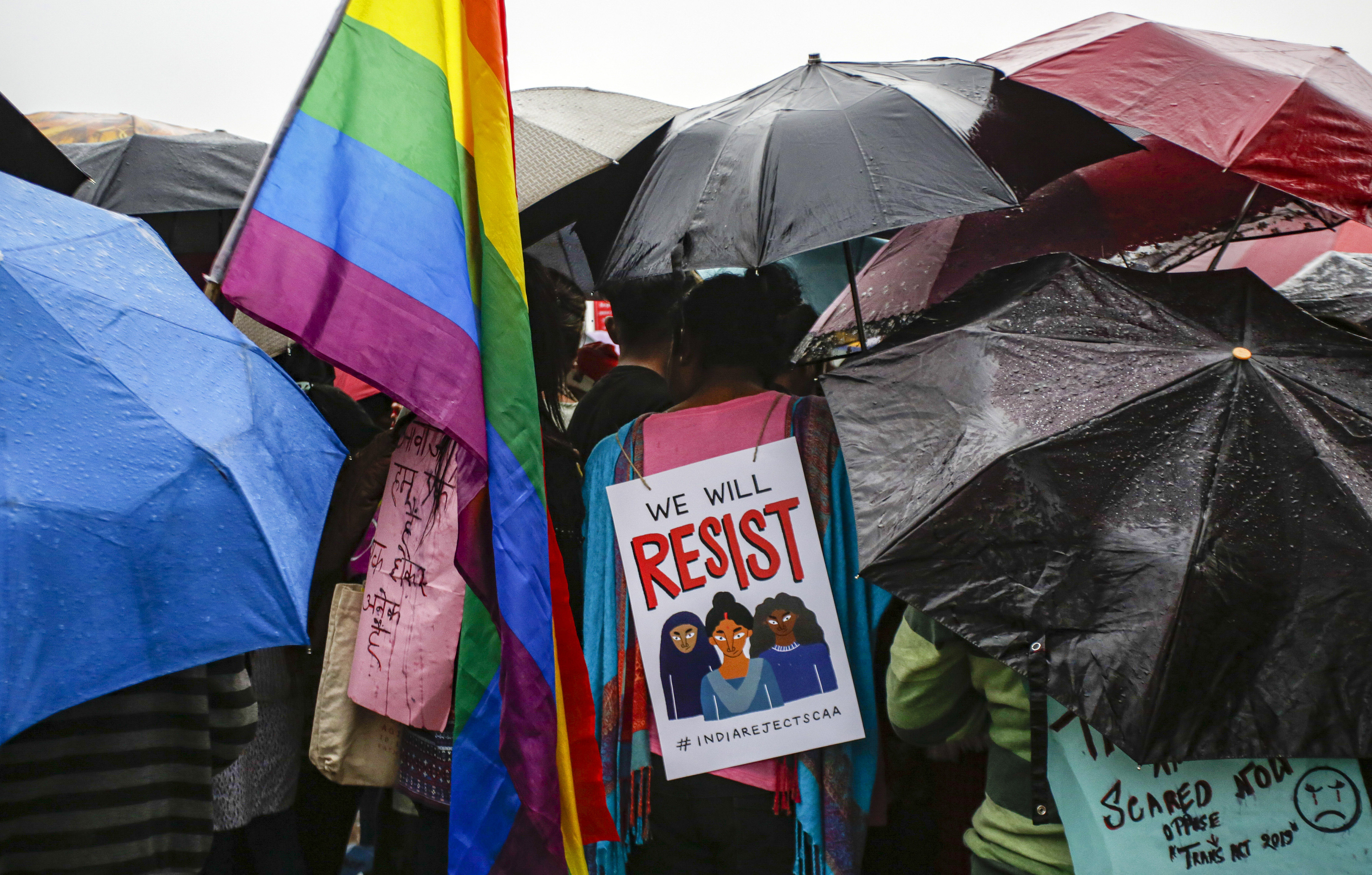 A member of LGBTQ community carries a placard while standing with others holding umbrellas as it rains during a rally to protest against the citizenship law that opponents say threatens India's secular identity, in Kolkata, India, Friday, January 3, 2020