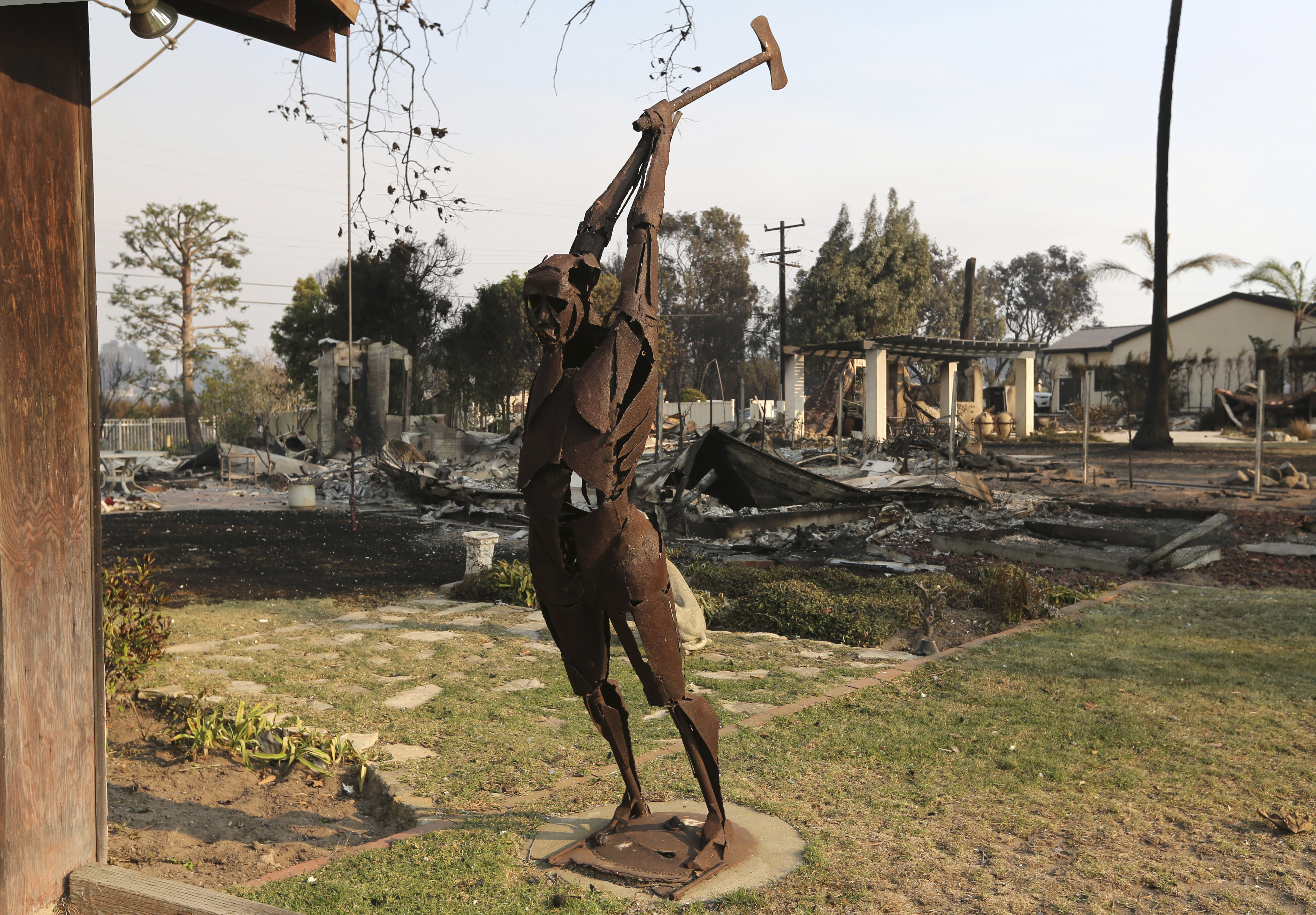 An iron figure stands in the yard of a home that survived, with others that did not in the background on Windermere Drive in Malibu.