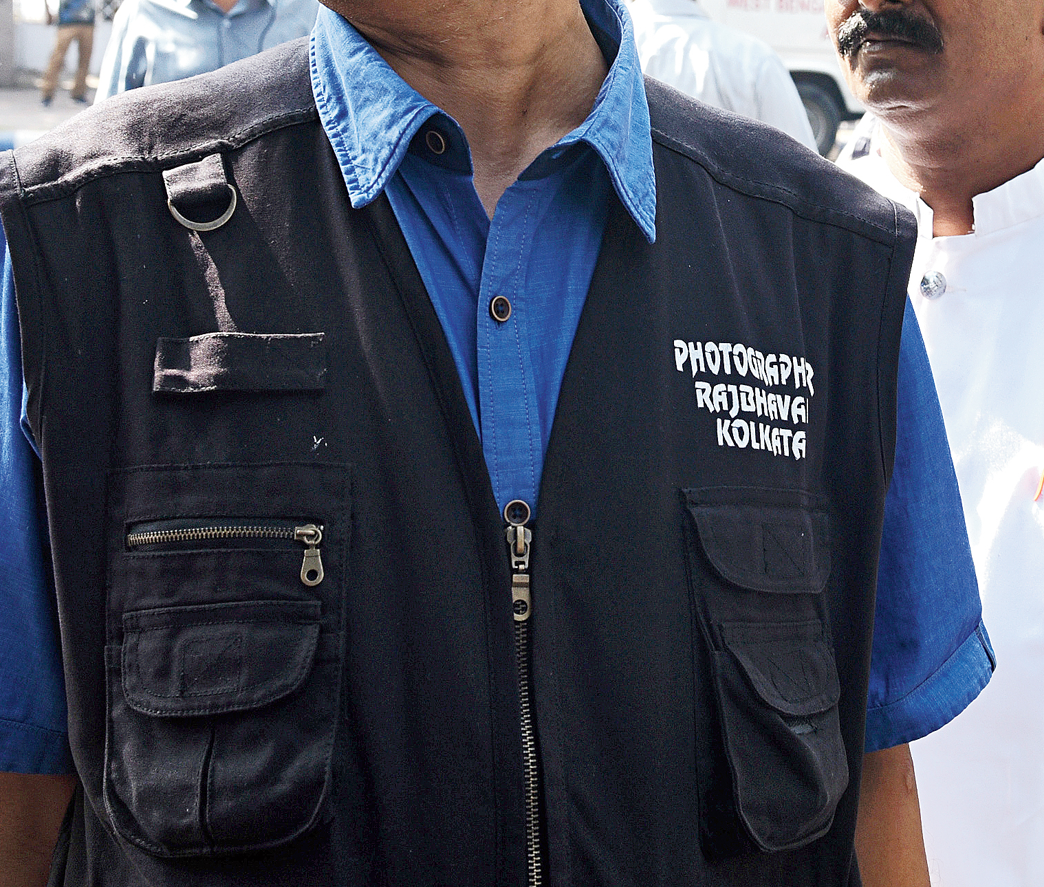 The photographer, whose  jacket says “Photographer Raj Bhavan Kolkata”, waits at the gate of the Assembly. 
