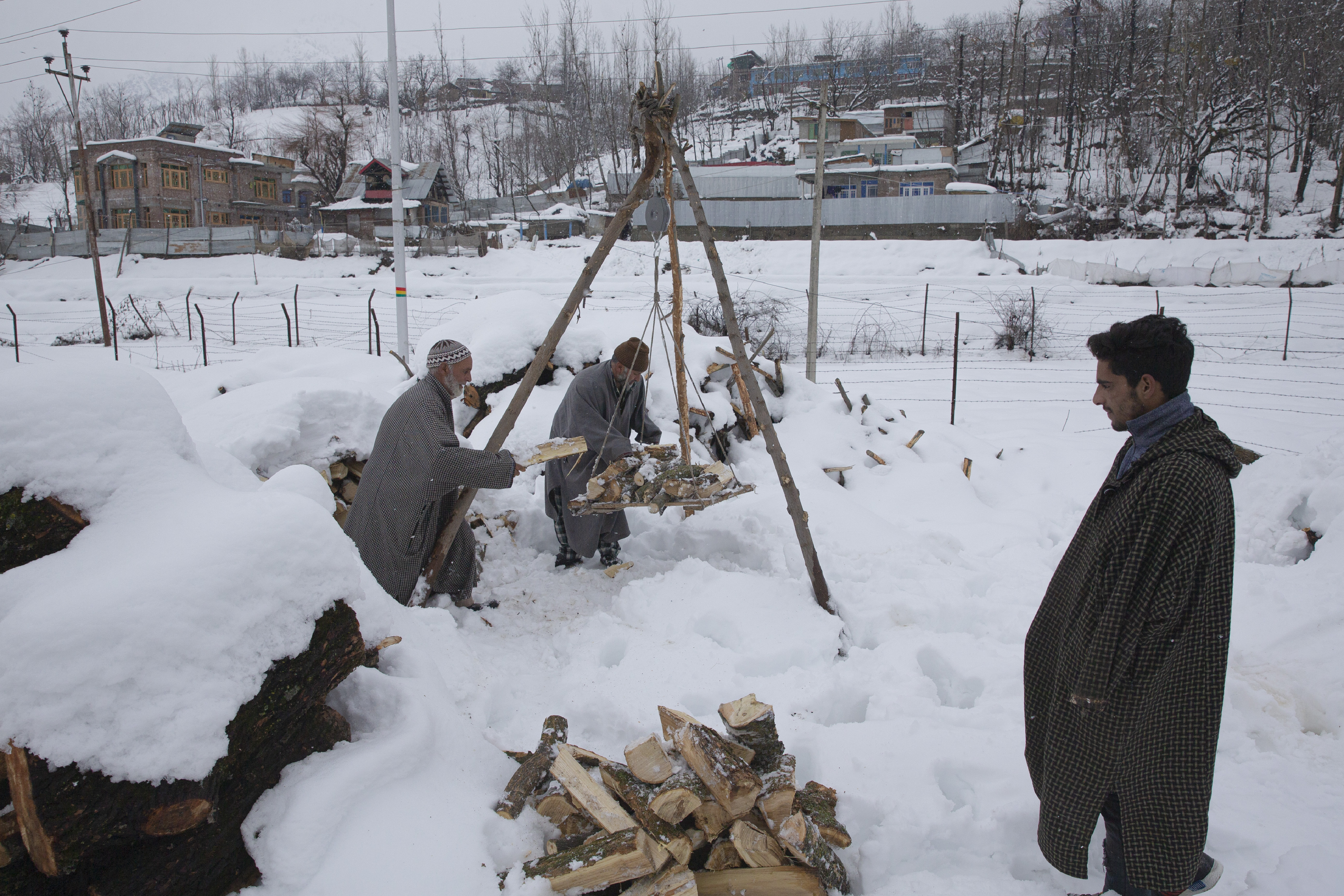 Kashmiri villagers load firewood buried under snow on a traditional weighing balance before selling it near Kangan village, north of Srinagar, Kashmir on Tuesday