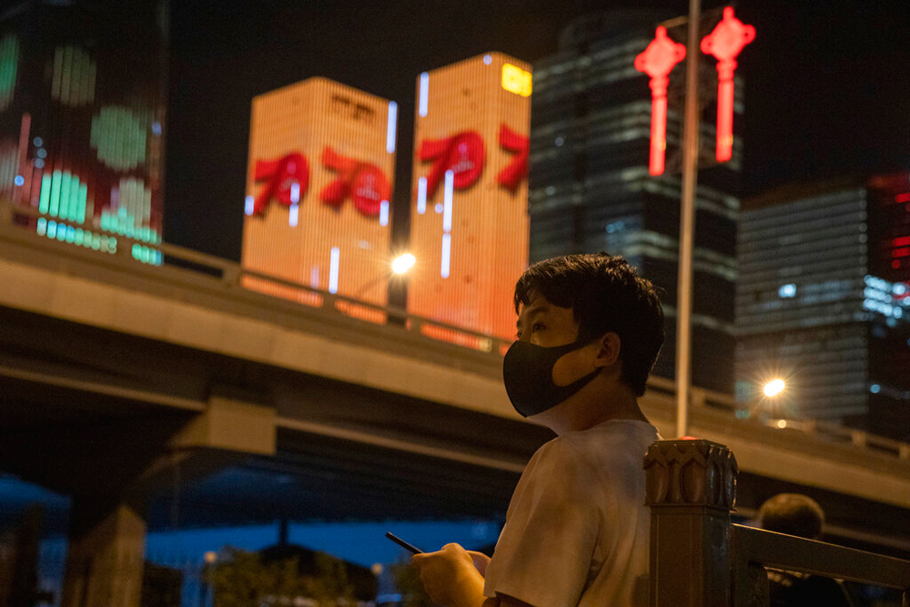 A resident wearing a mask stands near buildings lit up with the numbers 70 in Beijing on Friday