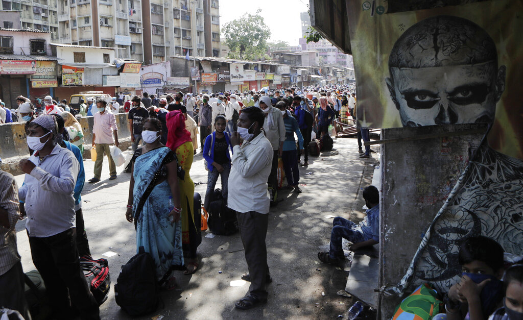 Migrant workers and their families gather for transport to the railway station for their onward journey to their home states, at Dharavi slum in Mumbai, on Tuesday, May 26, 2020
