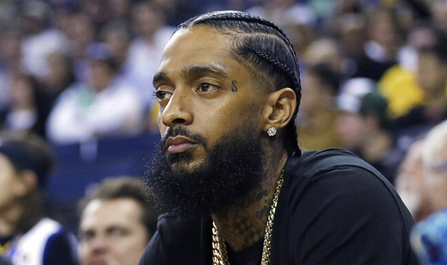 In this March 29, 2018, file photo, rapper Nipsey Hussle watches an NBA basketball game between the Golden State Warriors and the Milwaukee Bucks in Oakland, California.