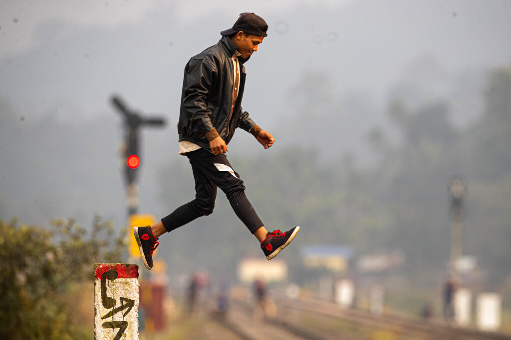 A boy jumps from a pole near a railway track after watching a herd of wild elephants graze in a forested area at Panbari village, on the outskirts of Gauhati, India, Tuesday
