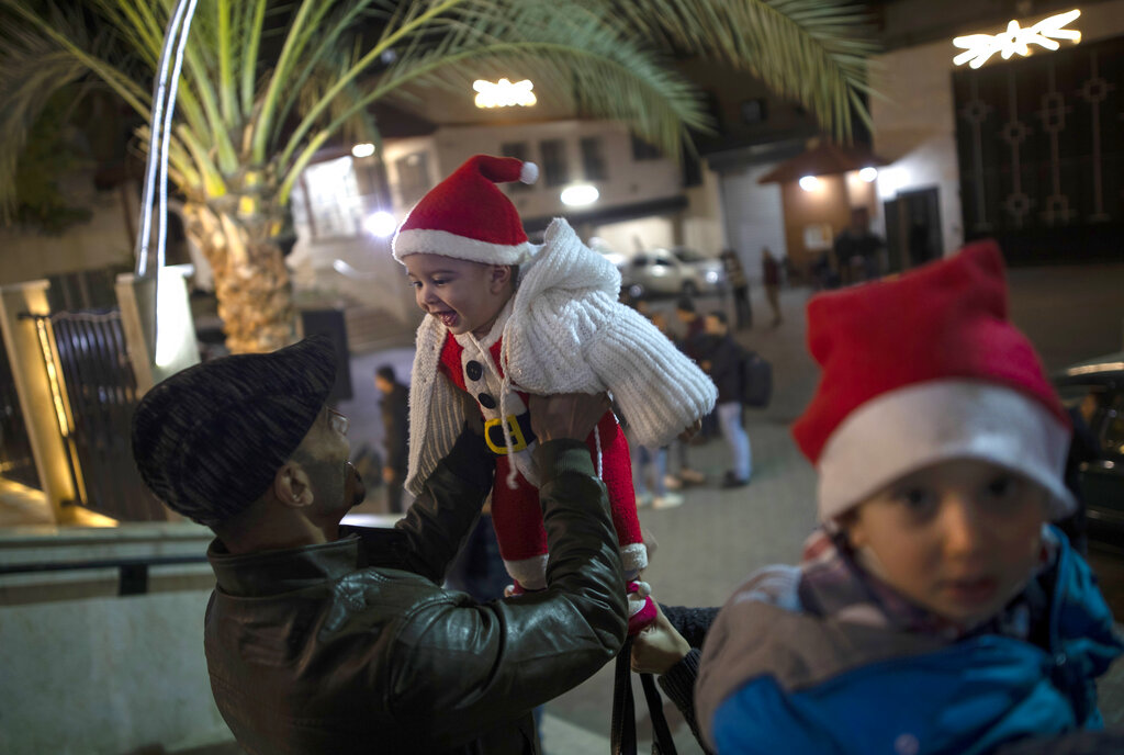 A Palestinian Christian man plays with his baby as they wait for the Christmas Mass outside the Holy Family Catholic Church in Gaza City, Tuesday, Dec. 24, 2019.