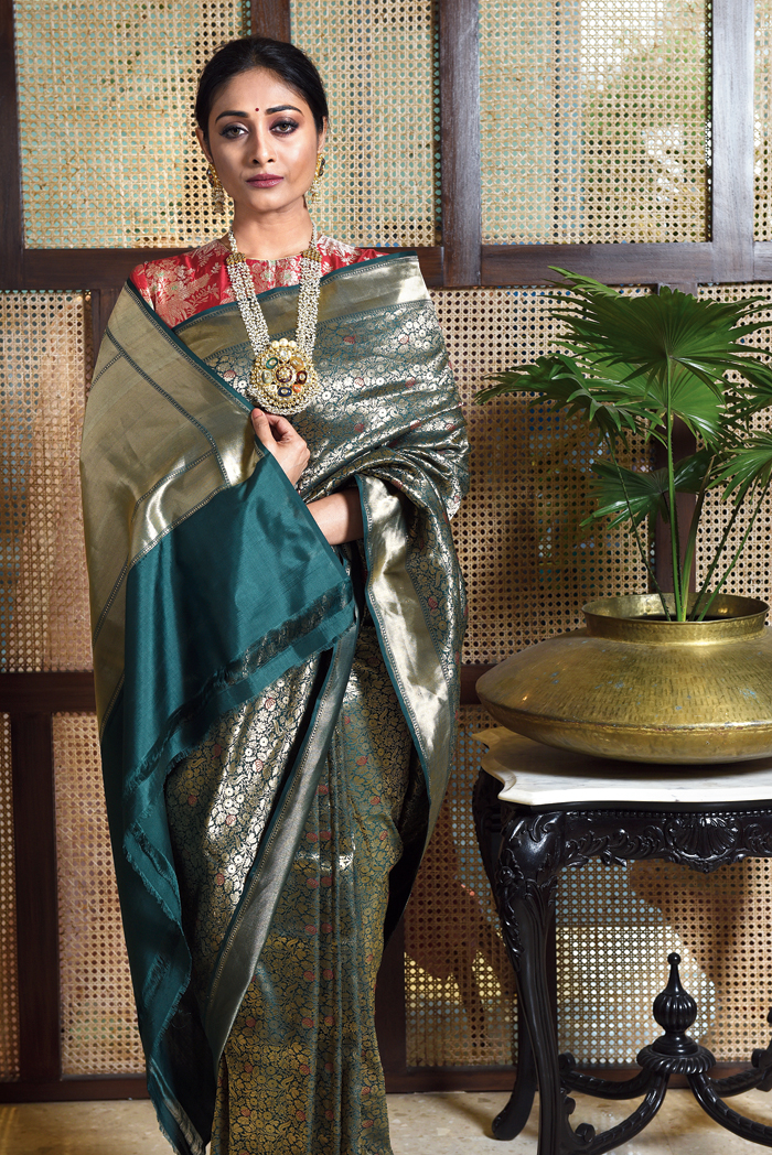 Elahe’s backdrop complements the minimal luminescence of this emerald green handwoven brocade sari paired with a red classic high neck blouse, both by Raw Mango. “The contrasting red blouse with a dark green golden embroidered sari from Raw Mango is the perfect reception look to enhance the after-glow of any bride,” said Ankita, who styled it with a long mala and dainty earrings. The centre-parted hair complements the small red bindi. Abhijit gave her soft brown eyes and subtle lips.