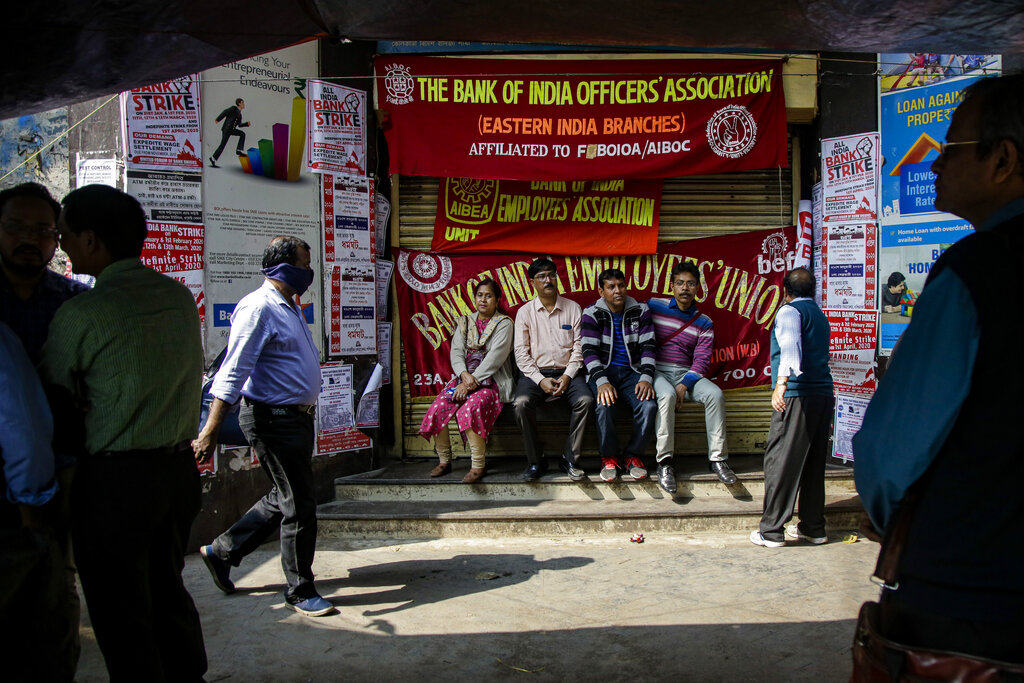 Employees sit in front of a closed bank during a two-day bank strike in Kolkata