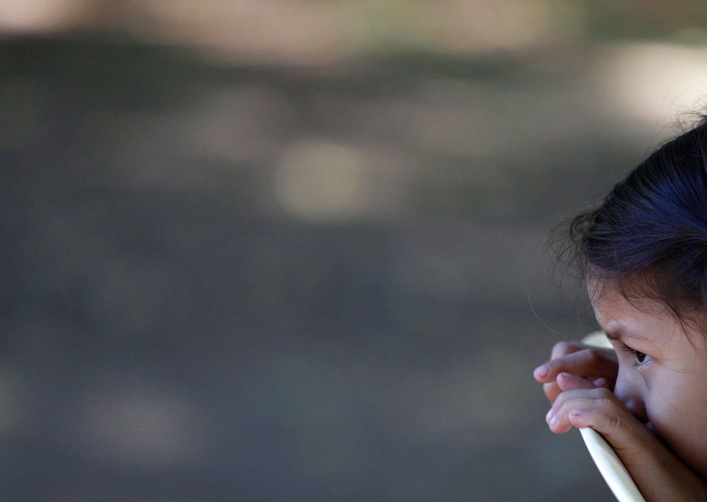 Alexa peers over the back of her chair as her mother speaks during an interview in a park in San Miguel, El Salvador.