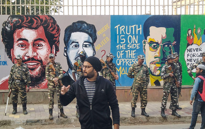 Security personnel stand guard in front of a wall painted with anti-CAA murals, outside Jamia Milia Islamia University in New Delhi, on Tuesday
