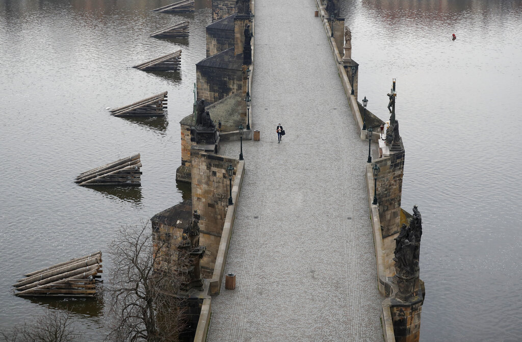 A woman walks across the near empty Charles Bridge in Prague, Czech Republic, Friday, March 20, 2020. The Czech Republic's government has approved further dramatic measures to try and stem the spread of the novel coronavirus called COVID-19. The Prague castle is in the background.