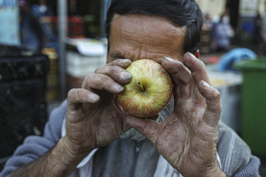 A homeless man jokes around using an apple to mimic the photographer at La Vega market in Santiago, Chile, Thursday, April 2, 2020, during a city-wide quarantine to help contain the spread of the new coronavirus. 