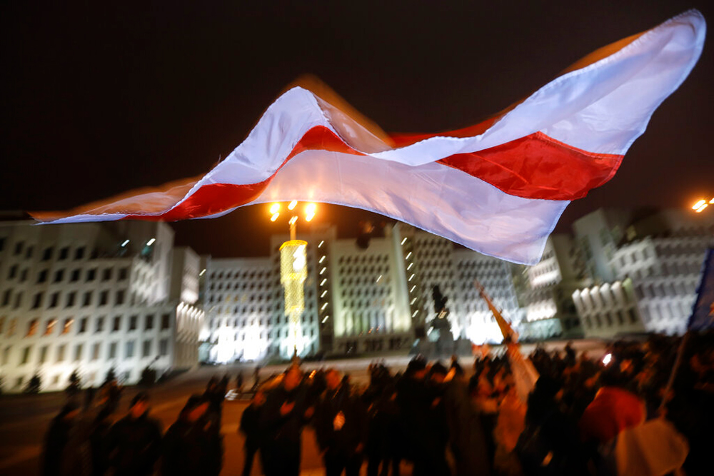 An old Belarusian flag flies over demonstrators during a rally to protest closer integration with Russia which the protesters fear could erode the post-Soviet independence of Belarus at Independent Square in Minsk, Belarus, on December 20