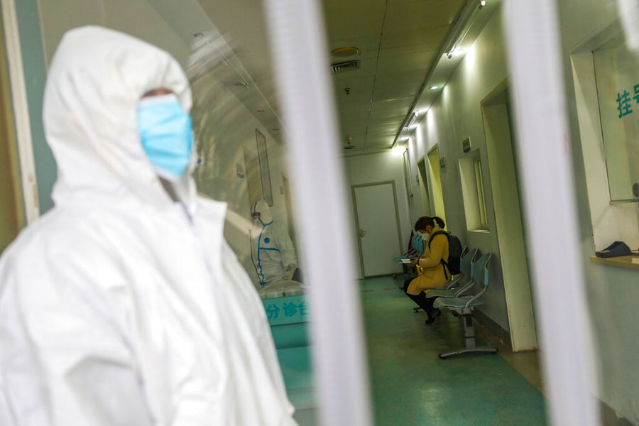 Medical workers in protective gear stand as a woman suspected of being ill with coronavirus waits to be seen at a community health station in Wuhan