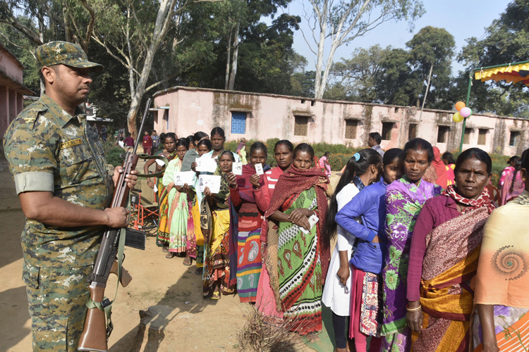 A trooper stands guard as people wait in a queue to cast their votes at a polling station in Lohardaga, Jharkhand, on Saturday 