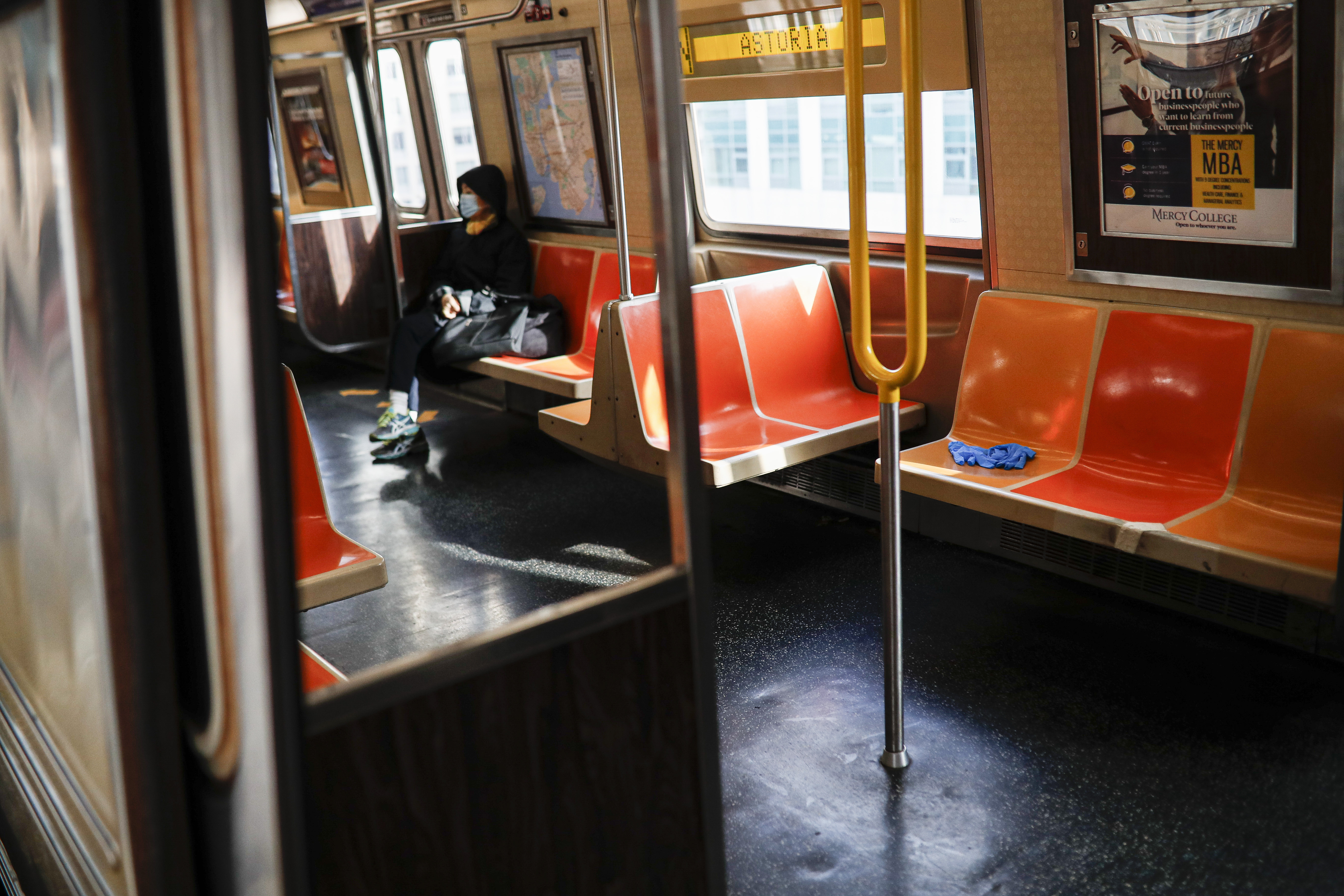 A pair of discarded gloves rests on an empty seat as a rider, wearing a mask as a protective measure over coronavirus concerns, uses the New York City subway system