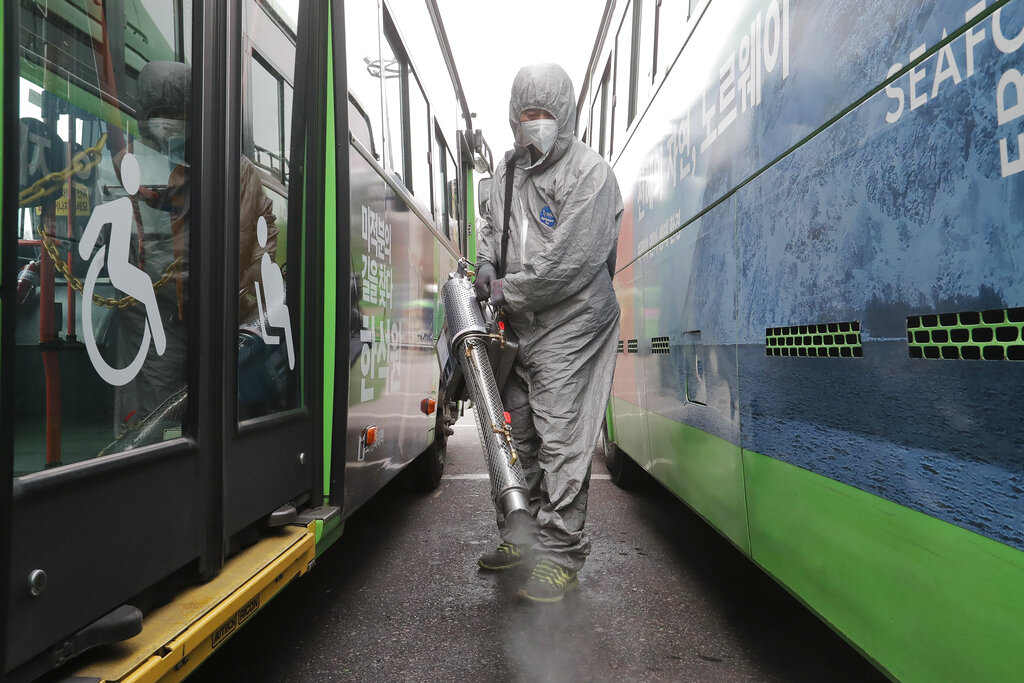 A worker wearing a protective suit sprays disinfectant as a precaution against the coronavirus at a bus garage in Seoul, South Korea