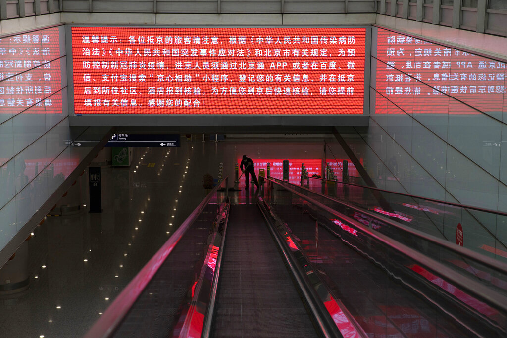 In this March 12, 2020, photo, a worker mops the area under a screening showing China's regulations related to the coronavirus outbreak at the Capital International Airport terminal 3 in Beijing. 