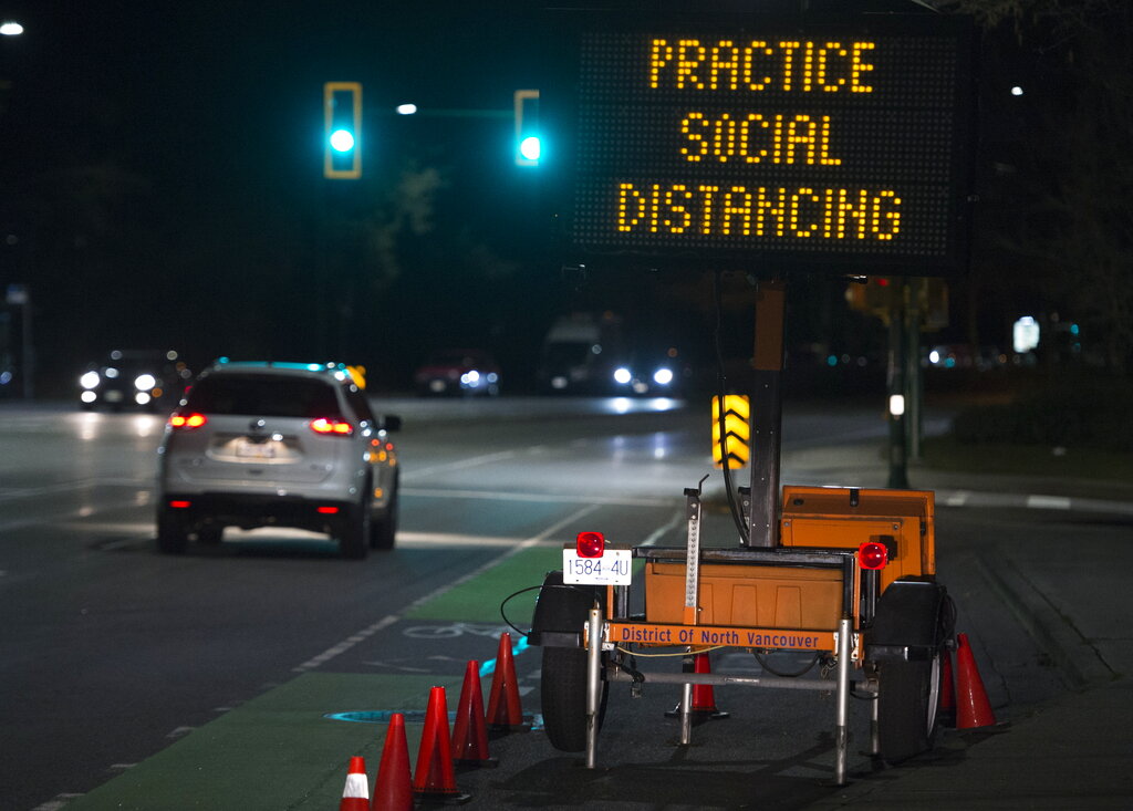 A sign reminding people about social distancing because of the coronavirus outbreak stands next to a roadway in North Vancouver, British Columbia, Wednesday, March 18, 2020