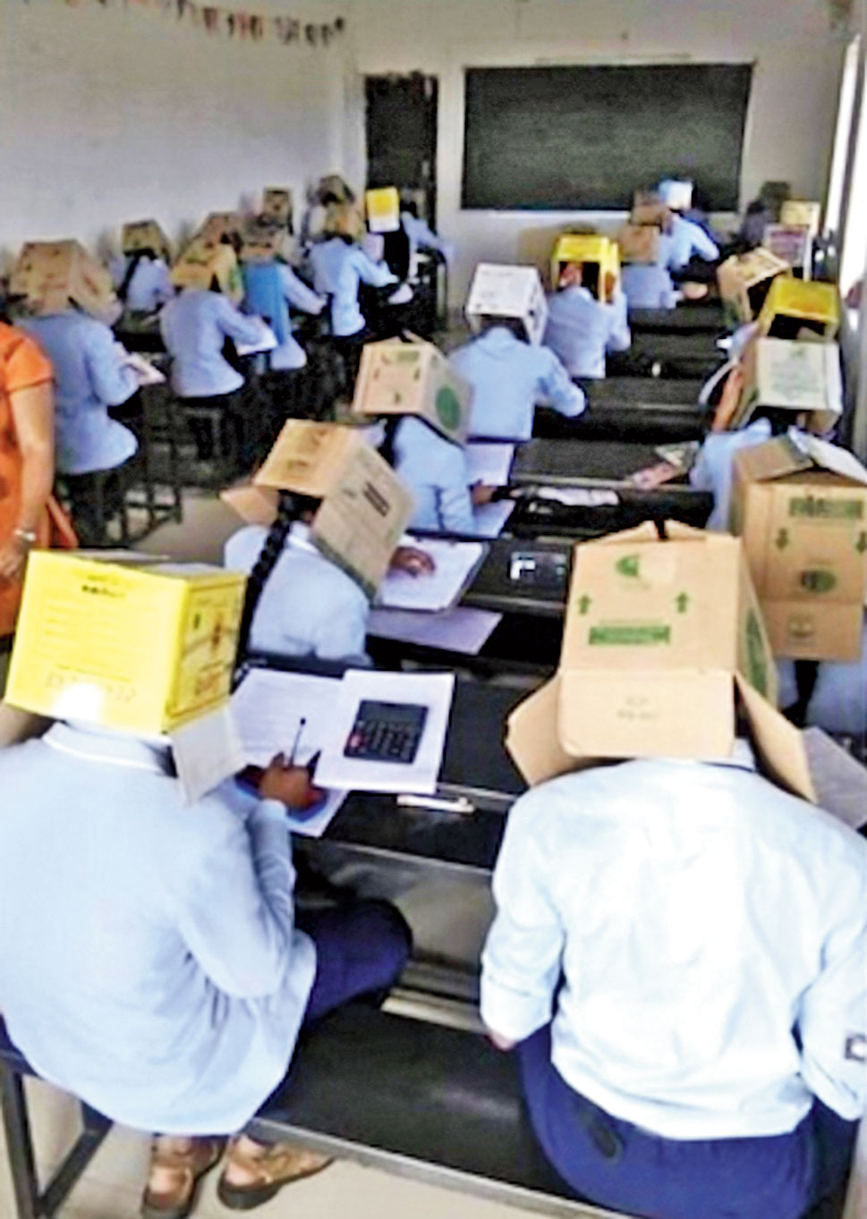 The students write the exam covering their heads with cartons in Haveri