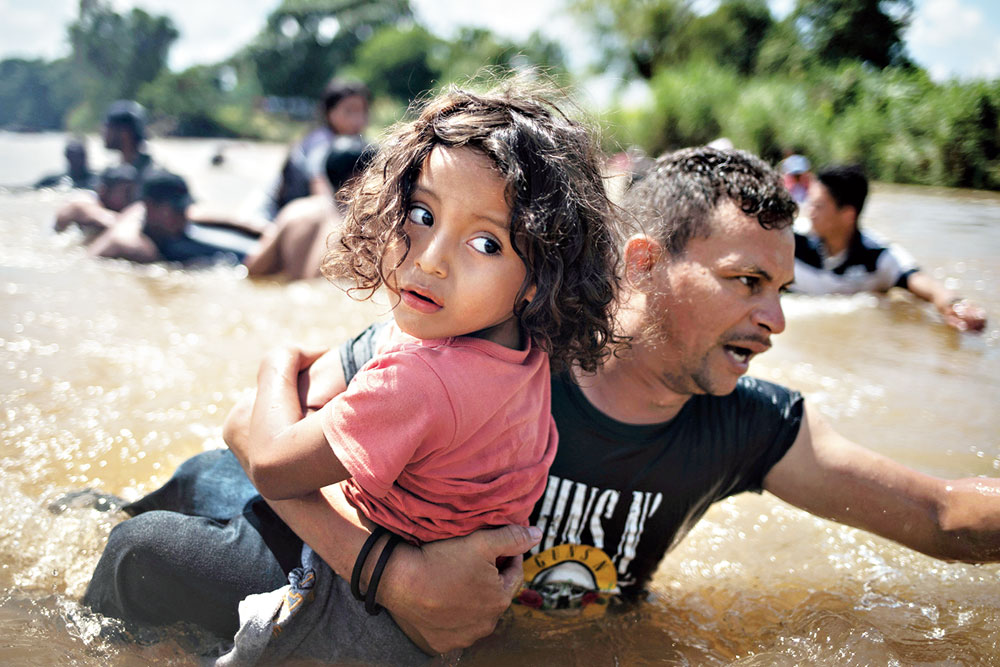 A man, part of a caravan of migrants from Central America en route to the US, carries a girl through the Suchiate river into Mexico from Guatemala. 
