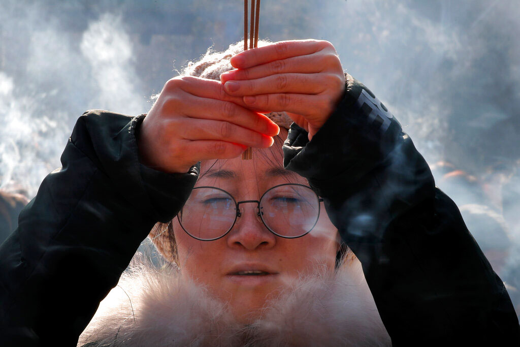 A woman holding incense sticks offers prayers on the first day of the New Year at Yonghegong Lama Temple in Beijing.