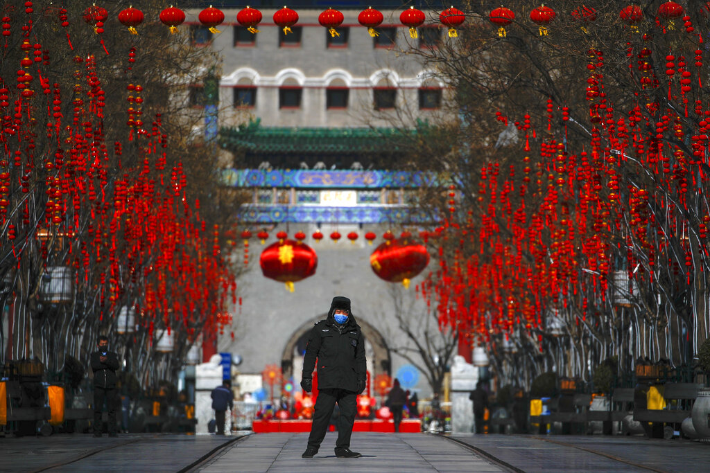A security guard wearing a face mask walks through a quiet main Qianmen Street, a popular tourist spot, in Beijing, Sunday