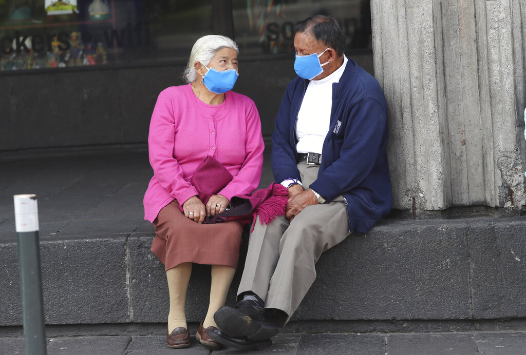A couple, wearing masks to prevent the spread of the new coronavirus, wait for someone at Independence square in Quito, Ecuador, Friday, April 3, 2020.