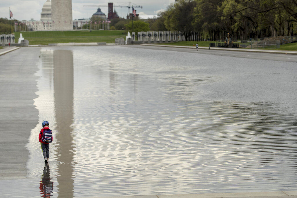 The Dome of the US Capitol and the Washington Monument are visible as Luke Shaw, 7, of East Falls Church, Va., gets off his bicycle to put his feet in the Reflecting Pool on the National Mall, Tuesday, March 31, 2020, in Washington. 