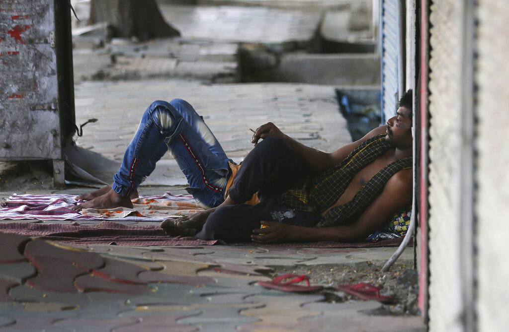 A homeless man sleeps as another smokes a bidi or hand-rolled cigarette as they spend time on a pavement during lockdown to prevent the spread of new coronavirus in Hyderabad, on Wednesday, April 22, 2020.