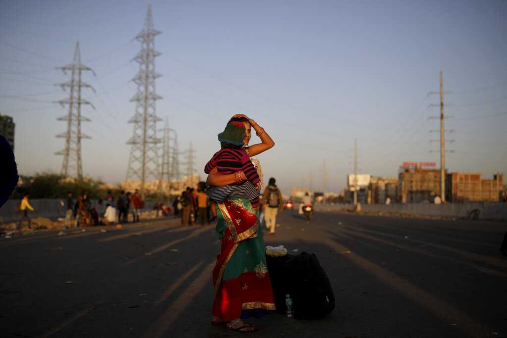 An Indian migrant worker holds a baby as she waits for transportation to her village following a lockdown amid concern over spread of coronavirus in New Delhi, on Saturday, March 28, 2020.