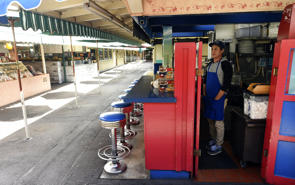 Ariel Nagbuya, an employee at The French Crepe Company, waits for customers in the sparsely populated The Original Farmers Market, Wednesday, March 18, 2020, in Los Angeles.