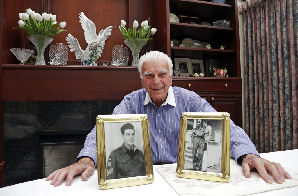 In this photo taken May 20, 2019, veteran Norman Harold Kirby sits with a photo of his mother, Katherine Louise Kirby, and himself, at 17, and a post-war portrait as he poses for a photo at his home in Lions Bay, Canada. The Canadian from British Columbia had joined the army when he was only 17 and was barely a 19-year-old private when he climbed into the landing craft that would take him to shore on June 6, 1944.