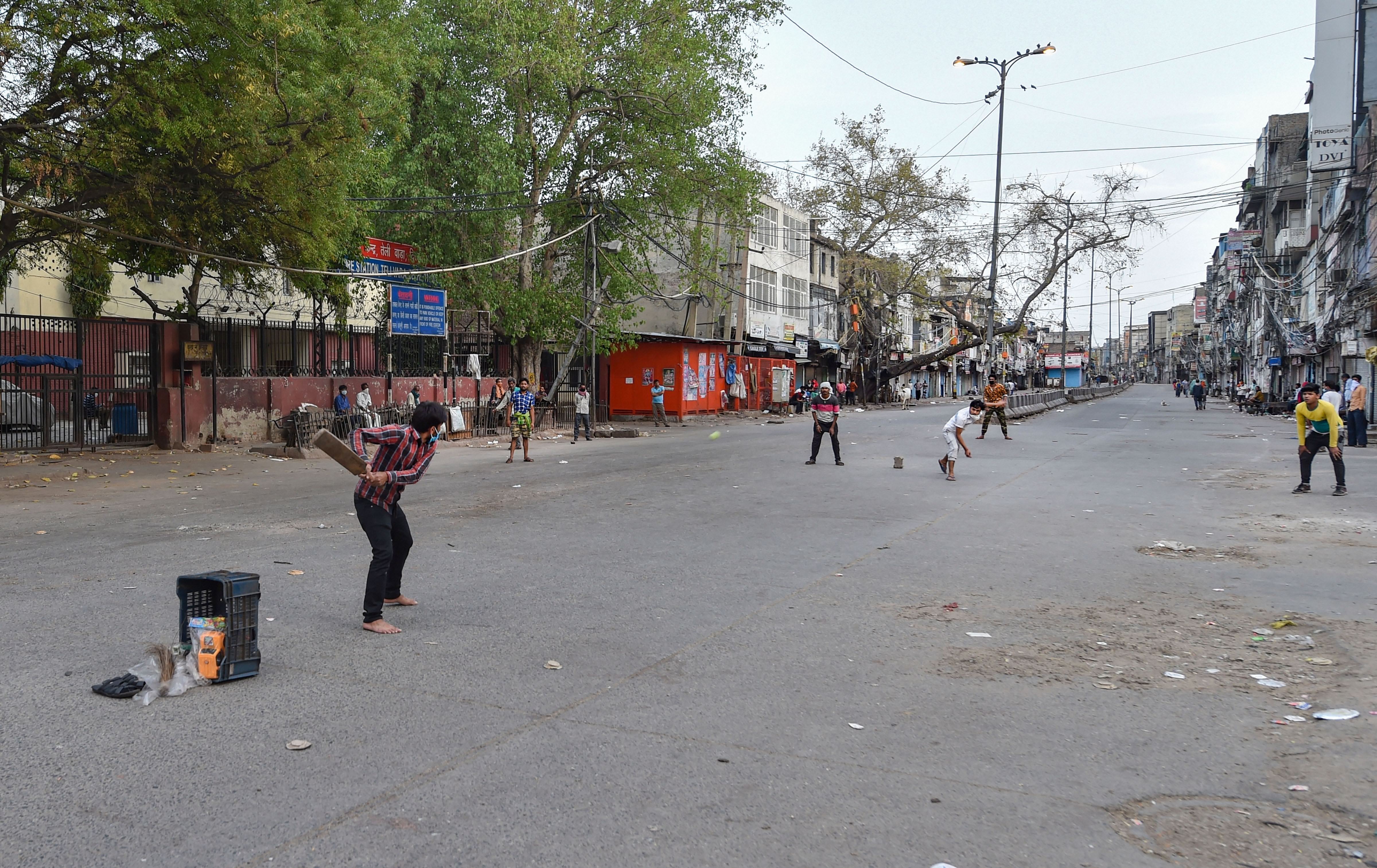 People play cricket on a deserted road at Sadar Bazar, during the nationwide lockdown imposed in wake of coronavirus pandemic, at Teliwara in New Delhi, Tuesday, April 7, 2020