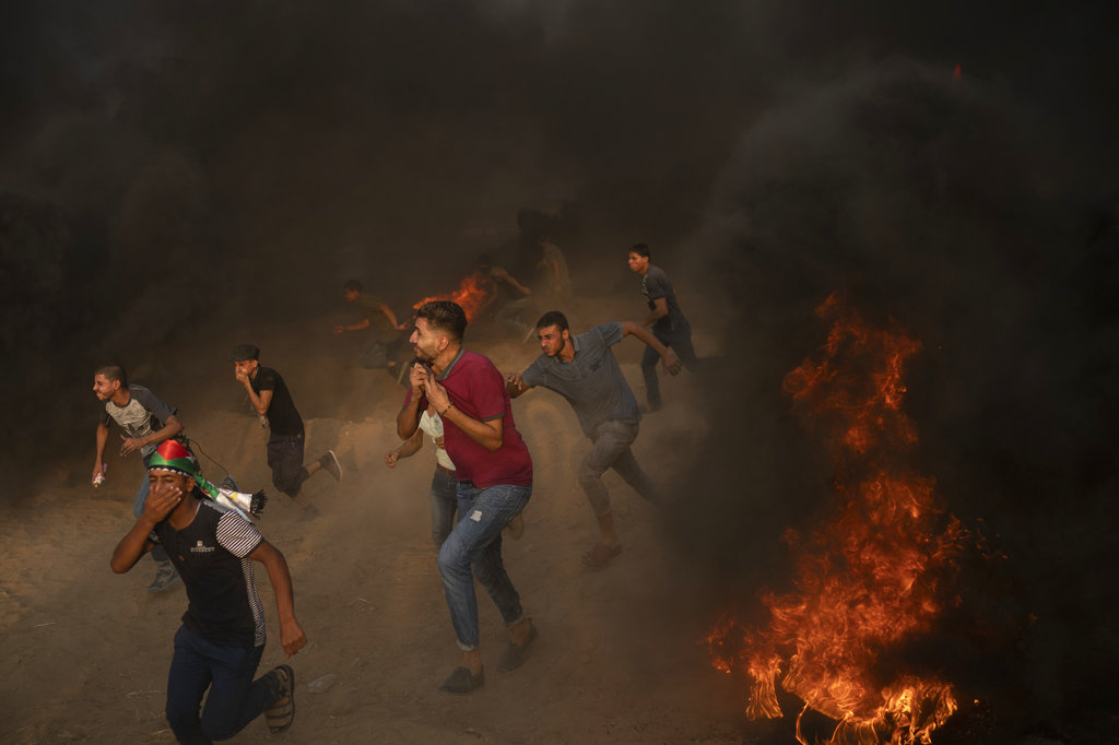 Palestinian protesters run from teargas fired by Israeli troops during a protest at the Gaza Strip's border with Israel, east of Gaza City. The noise here is constant, like a waterfall. Men blow whistles, others scream at the top of their lungs.